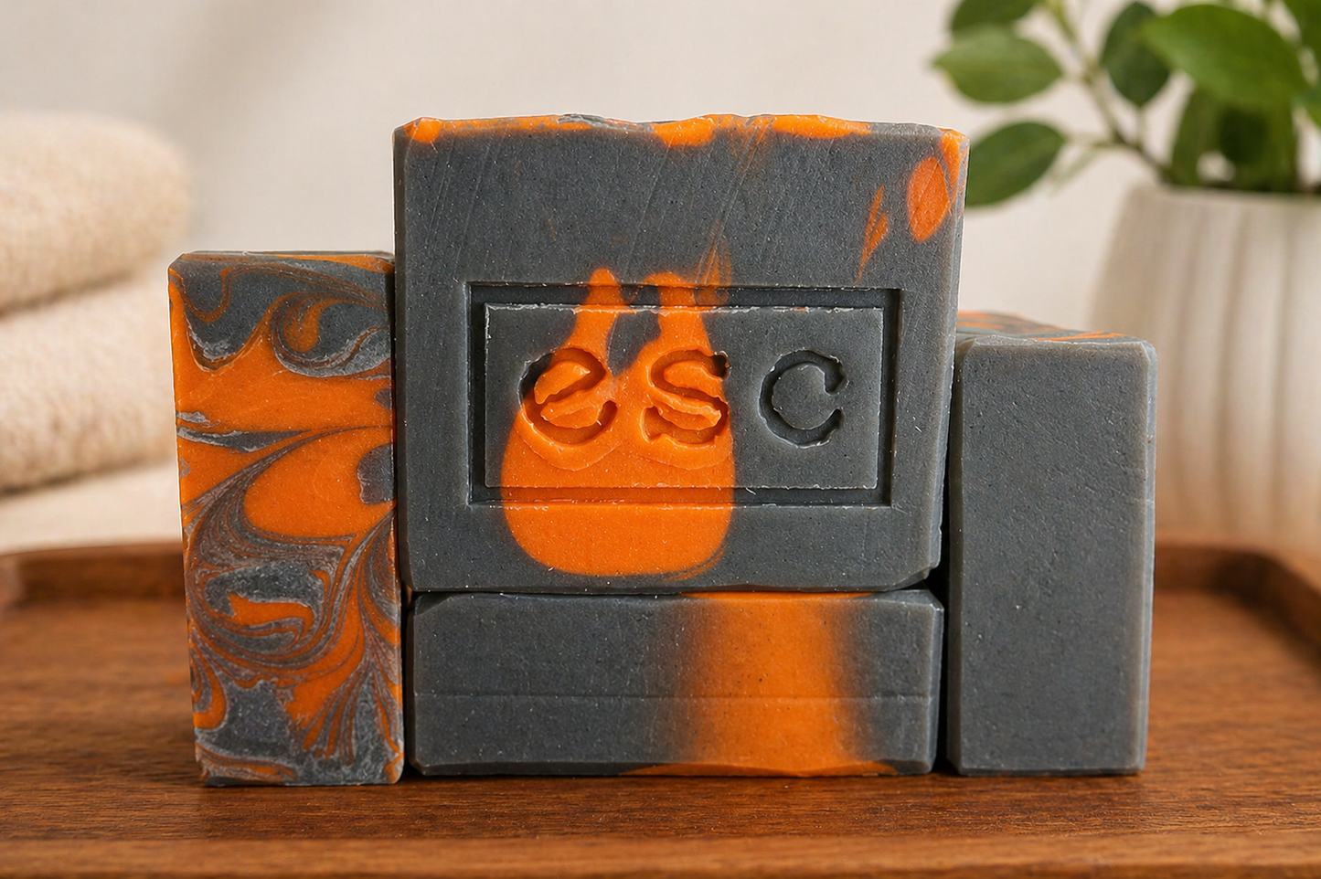Four bars of soap with a orange and grey marbled design on a wooden surface, featuring the brand 'ESC', which is the logo for Euphoros Soap Company.