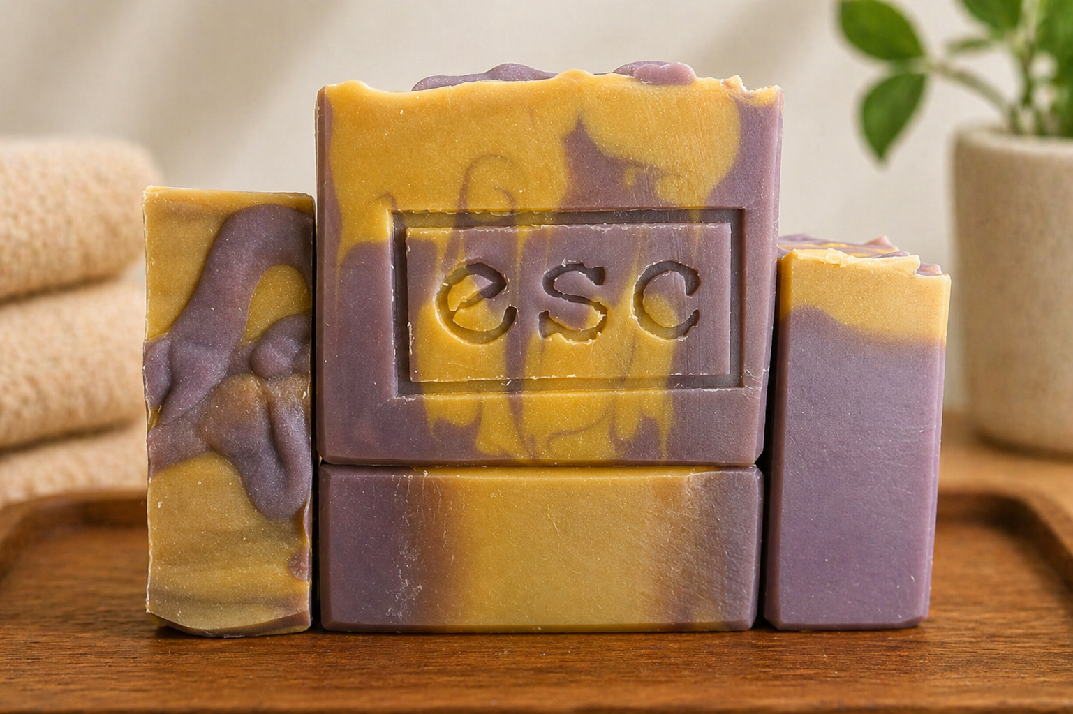 Four bars of soap with a purple and yellow marbled design on a wooden surface, featuring the brand 'ESC', which is the logo for Euphoros Soap Company.