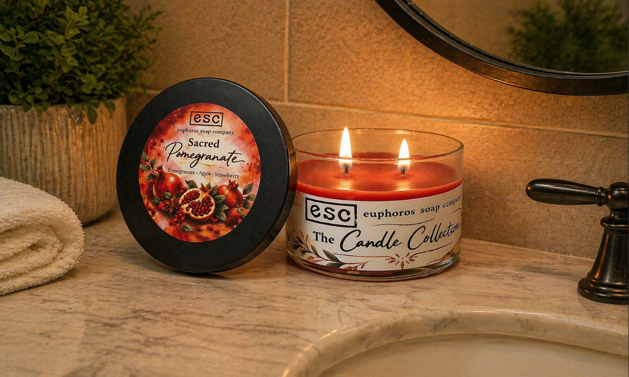 Red candle and container with 'euphoros soap company' branding on a bathroom counter.  The candle has two wicks that are lit.